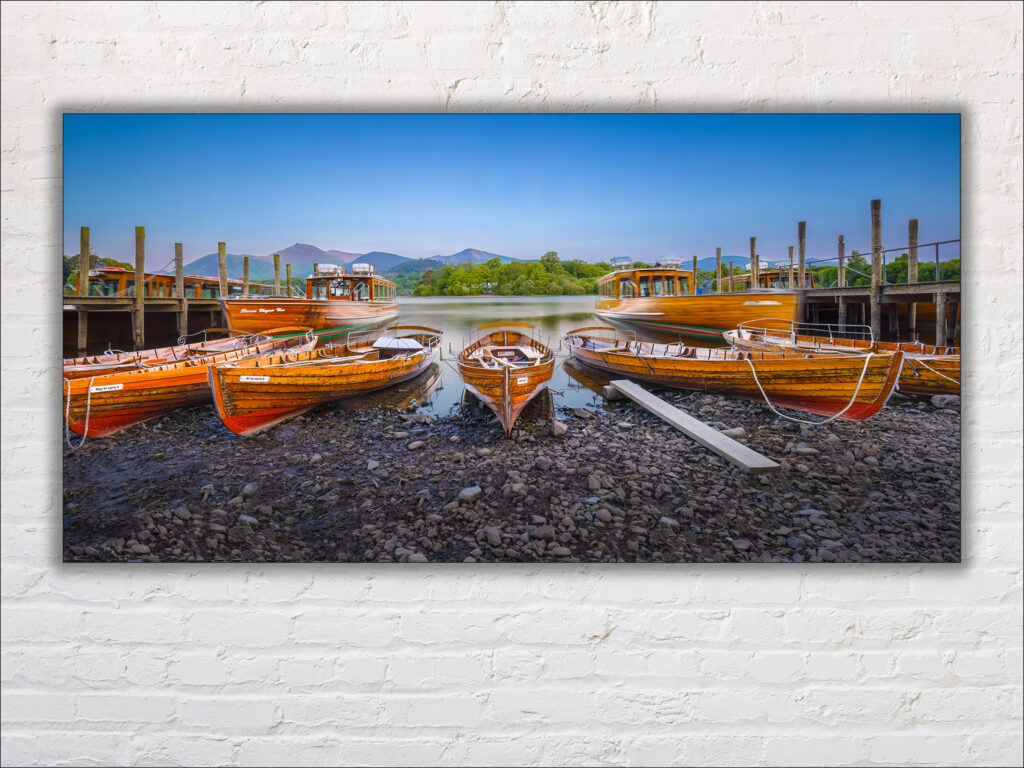 Wooden rowing boats at the Keswick Boat Landings, Derwentwater, Lake District. Shown here as a print mounted on a white brick wall.